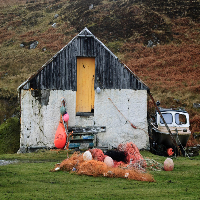 Boat House with boat to the right and orange fishing nets and bouys in front